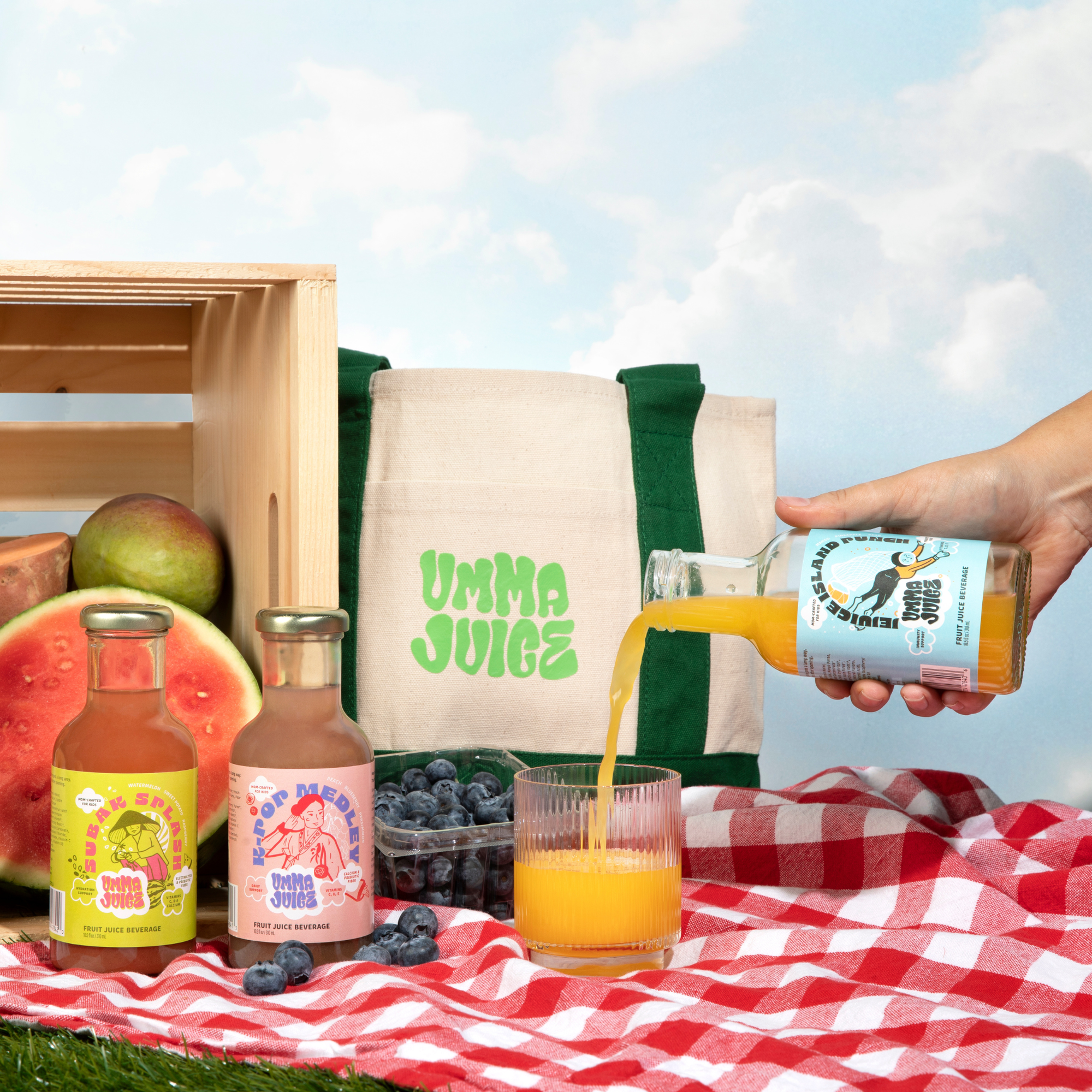 Person pouring juice from a bottle labeled 'UMMA JUICE' into a glass on a picnic setup with fruits and a branded bag.