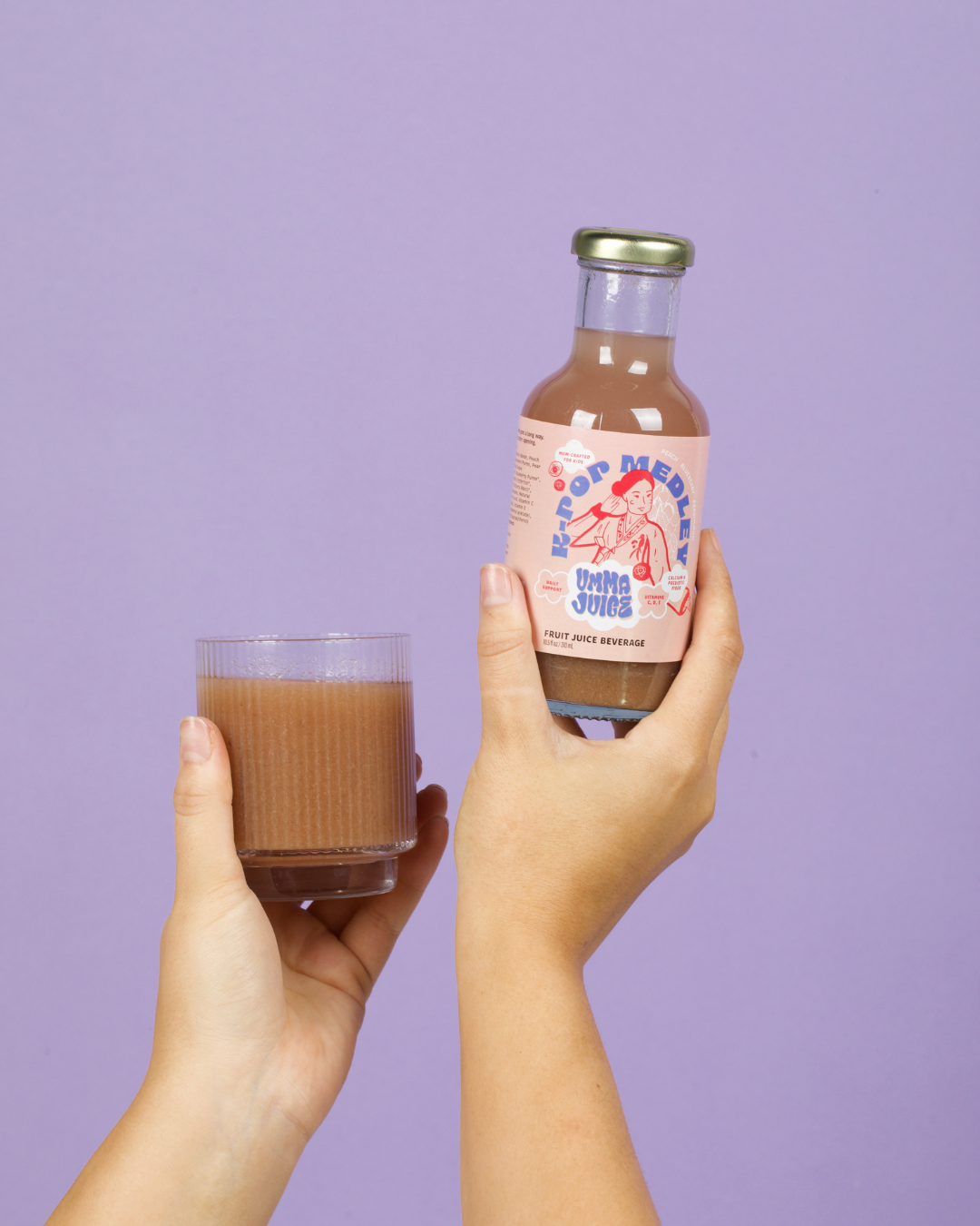 K-Pop Medley juice bottle and glass of juice held by hands against a purple background